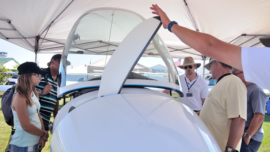 AirVenture attendees look at the Stemme S12 motorglider's cockpit. A Stemme dealership representative holds a propeller blade in the extended position; the blades retract when the engine is shut off.