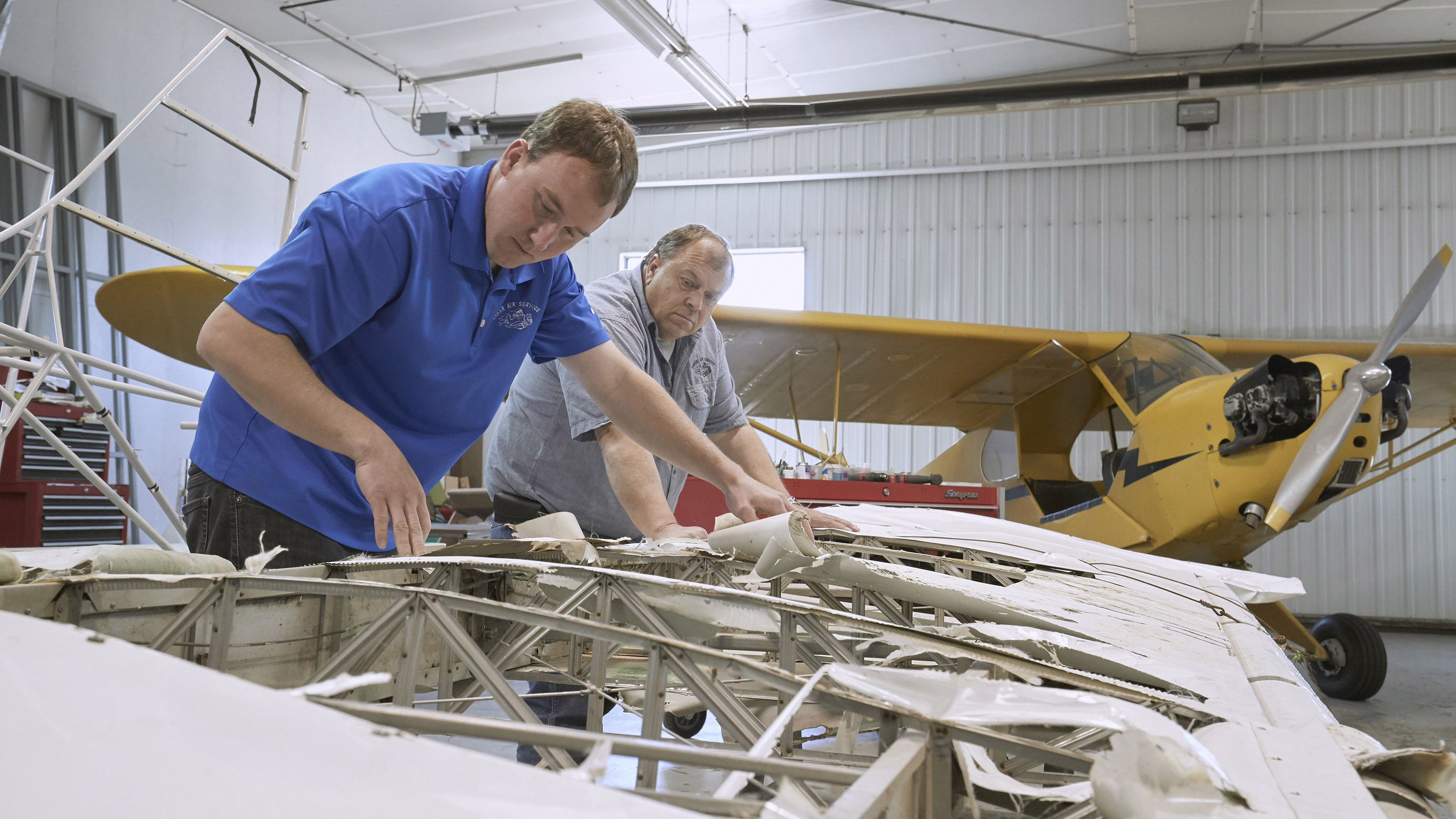 Darin (front) and Roger Meggers inspect the Piper Super Cub's damaged wings. Photo by Mike Fizer.