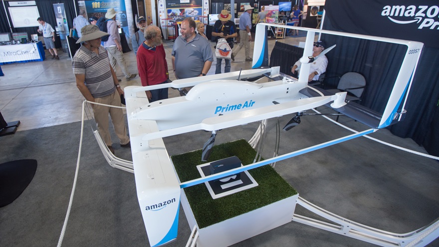 Amazon Prime Air Director of Manufacturing, Integration & Optimization Russell Williams (center, gray shirt) chats with a visitor to the company display at EAA AirVenture in July. The company is among those that have conducted research and testing in foreign countries due to regulatory restrictions that the White House now seeks to ease. Jim Moore photo.