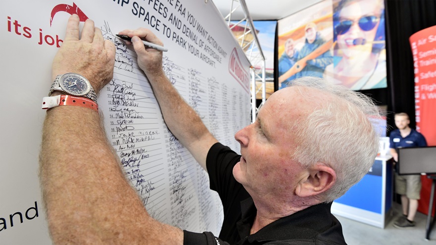 AOPA President Mark Baker signs AOPA's petition asking the FAA to address egregious FBO pricing, following a panel discussion on the topic at EAA AirVenture 2018. Photo by Mike Collins.