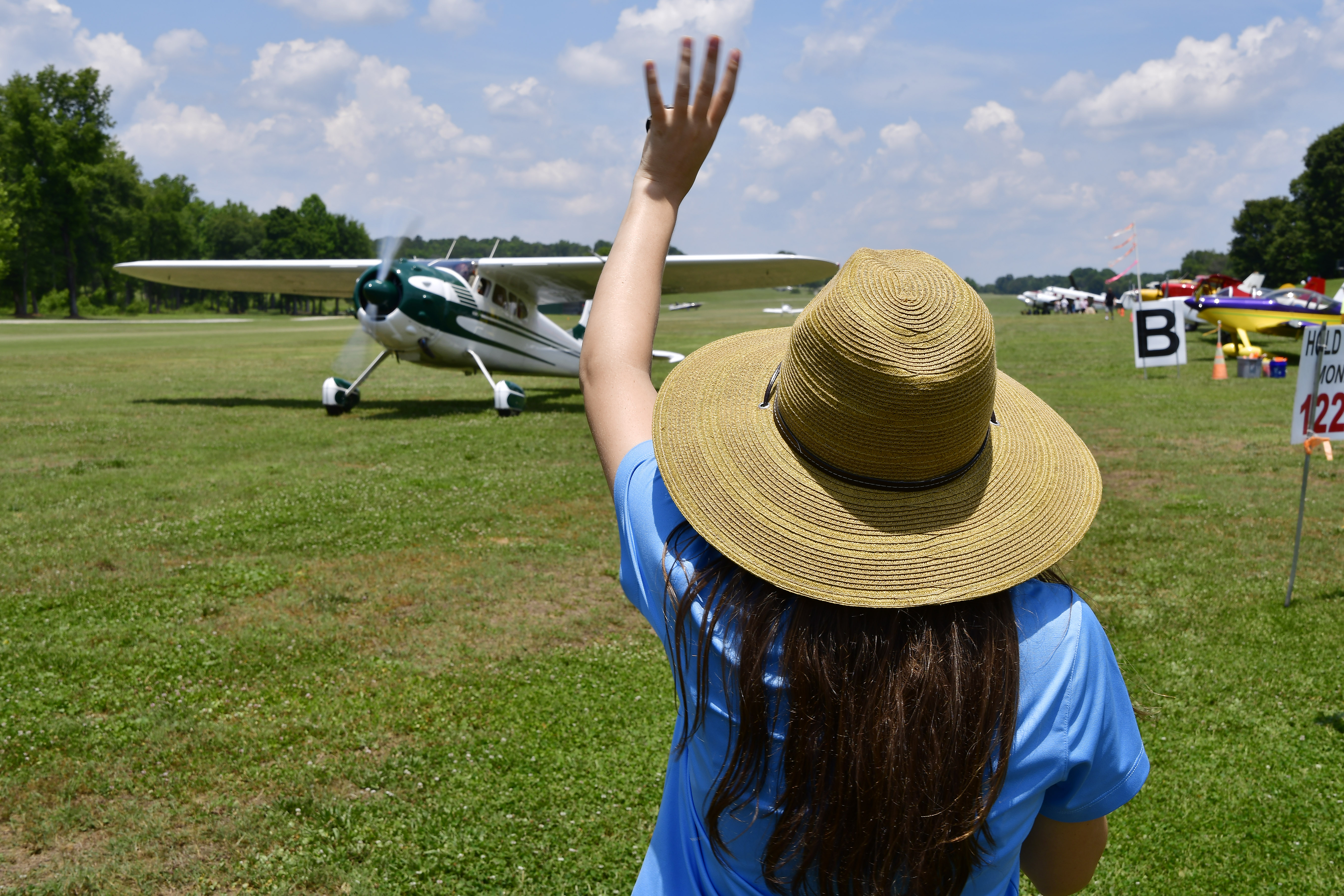 Cayla McLeod waves goodbye to a departing Cessna 195 pilot during the Young Aviators Fly-In at Triple Tree Aerodrome in Woodruff, South Carolina, June 8 to 10. Photo by David Tulis.
