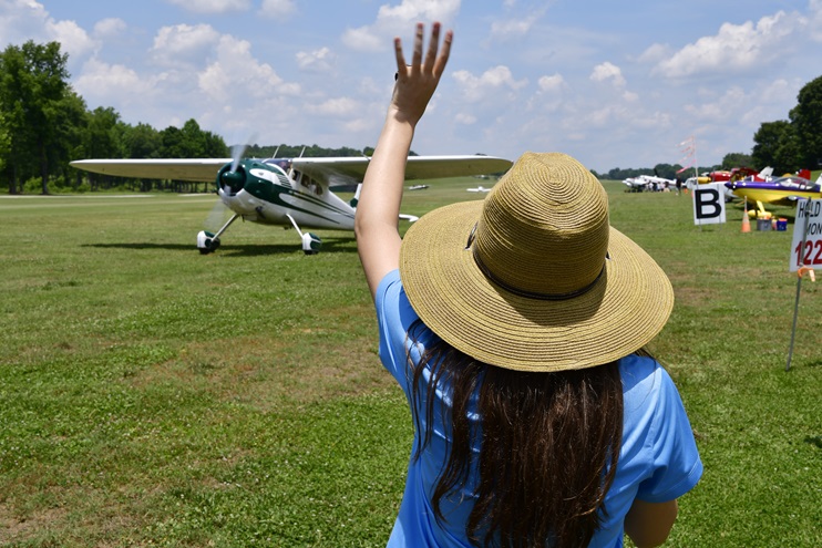 Young Aviators Fly-In co-founder Cayla McLeod waves at a departing Cessna 195 pilot during the inaugural event at Triple Tree Aerodrome in Woodruff, South Carolina. Photo by David Tulis.