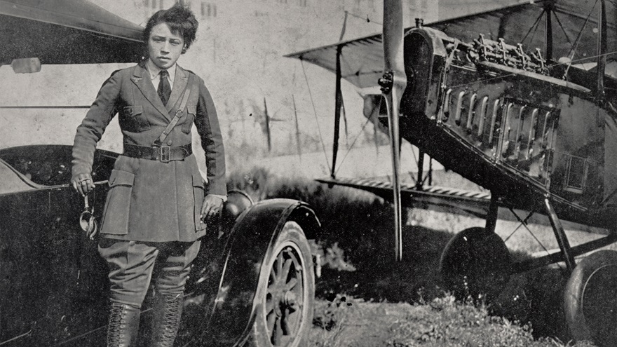 Bessie Coleman in tailor made officer's uniform posed standing on the running board of a Ford Model T automobile with nose and right wing of her Curtiss JN-4 Jenny to her left. Photo courtesy of Smithsonian’s National Air and Space Museum.