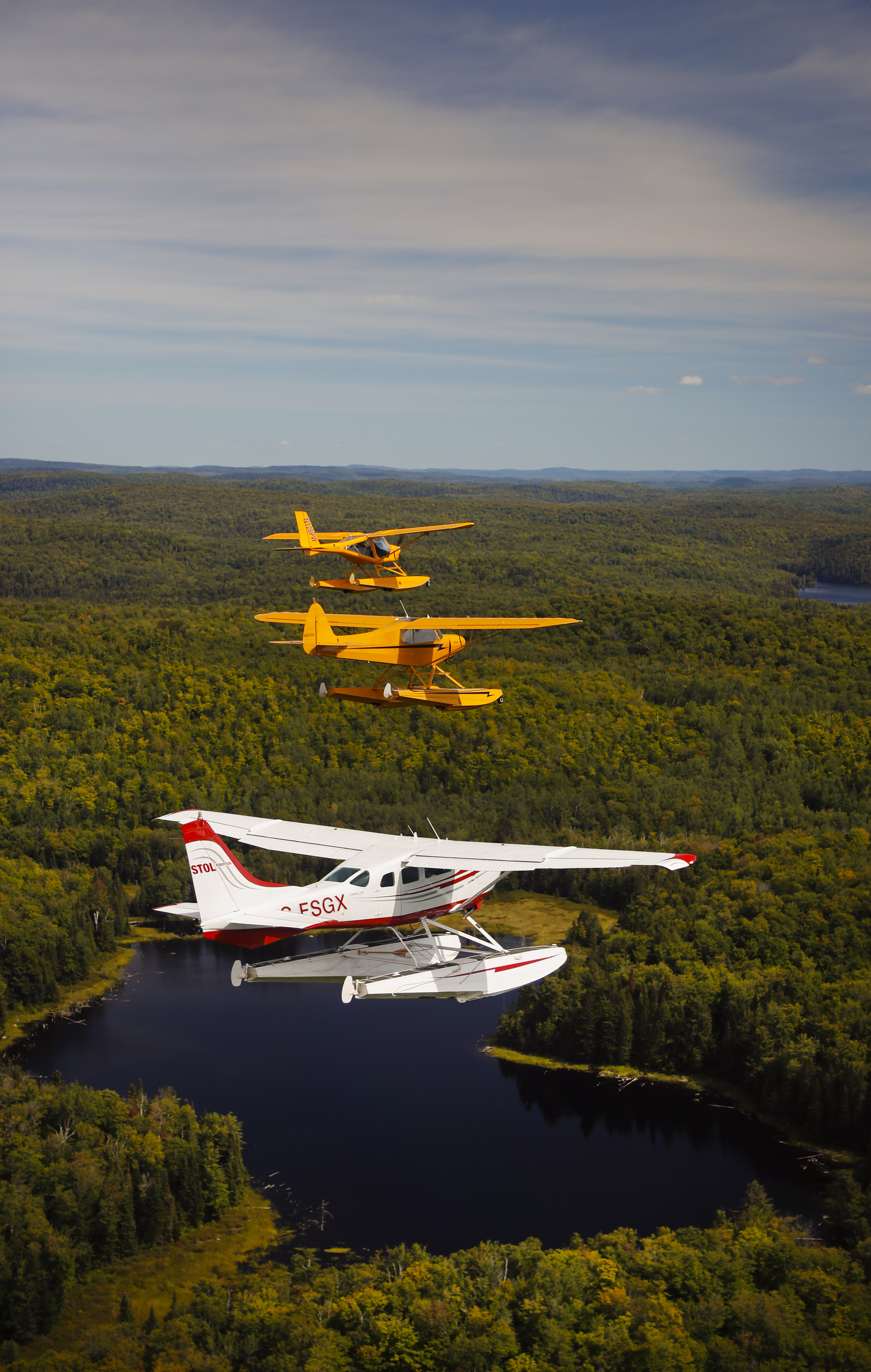 The slow airplane leads: an Aeroprakt A–22 sets the pace for a Super Cub and Cessna 206 Stationair on floats to follow. 