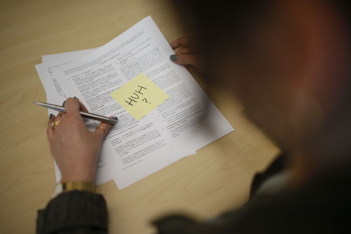 Photo of female hands signing Insurance form with a Post-It note reading "Huh?"