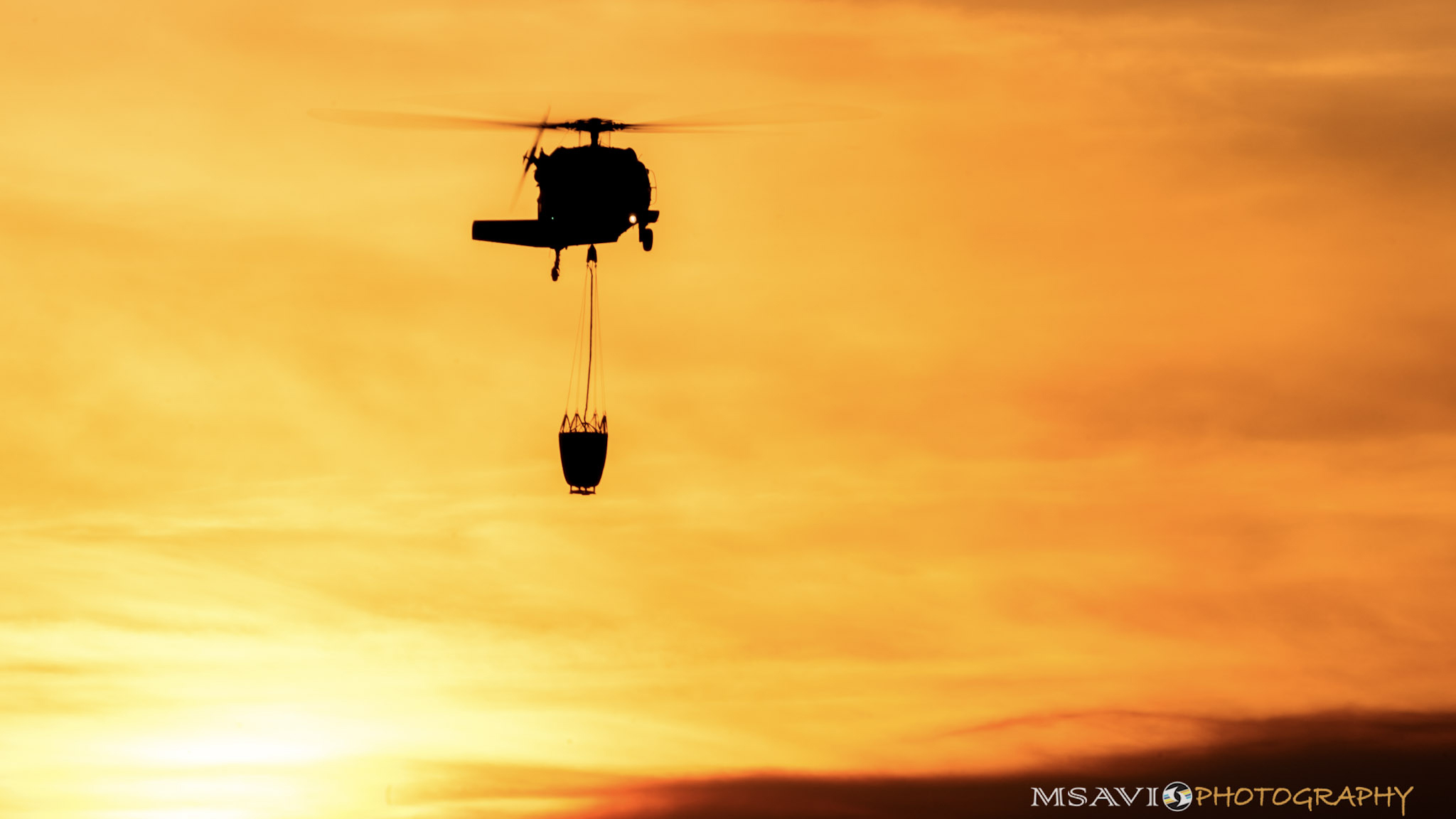 The sun frames a helicopter carrying a bucket during firefighting operations based at California's Santa Paula Airport. Photo by Mike Salas, MSAVI Photography and Focal Flight.