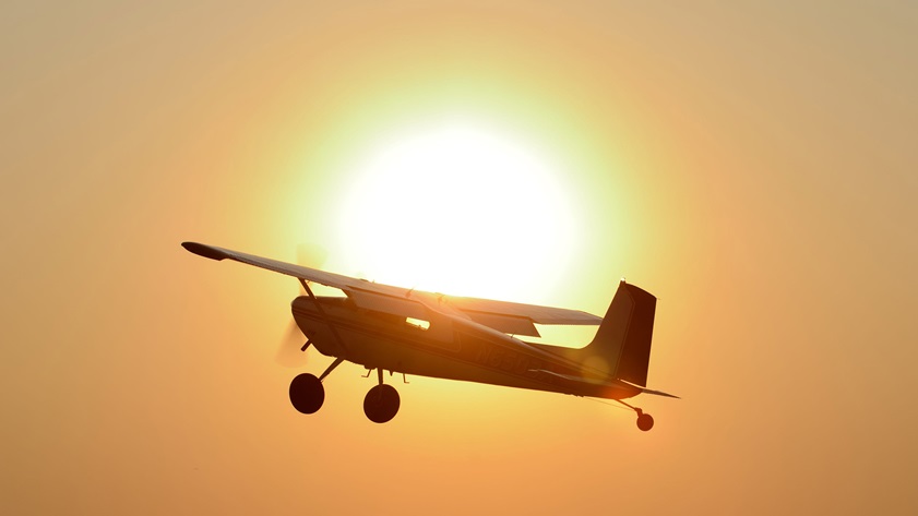 A Cessna 180 climbs past the setting sun during the short takeoff and landing (STOL) demonstration held Friday evening at AOPA's 2017 Norman Fly-In. Photo by Mike Collins.