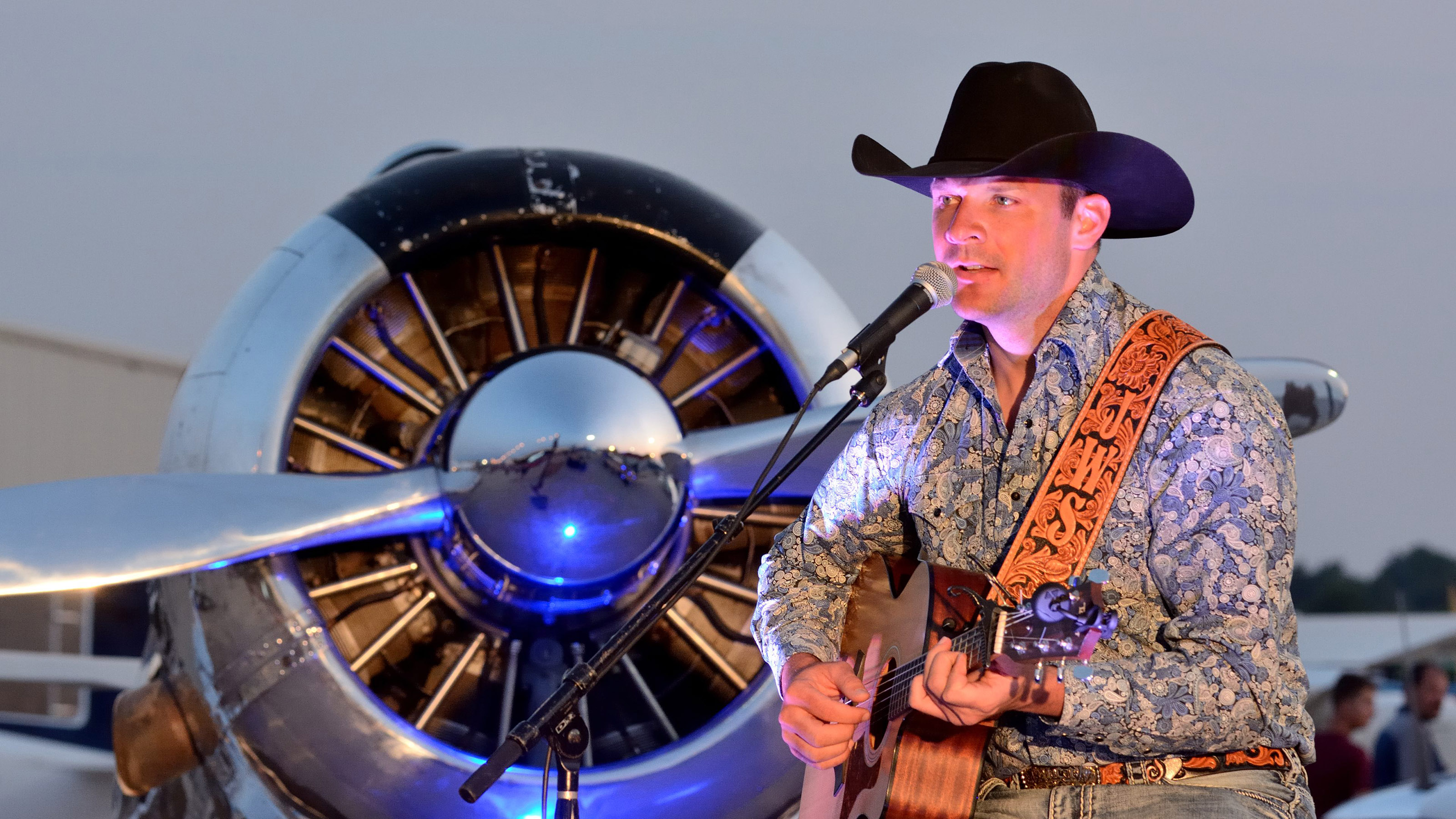 Country singer John Wayne Schulz--who also is a pilot and an active flight instructor--entertains the crowd during Friday evening's Barnstormers Party at AOPA's 2017 Norman Fly-In. A North American T-6 serves as the backdrop. Photo by Mike Collins.
