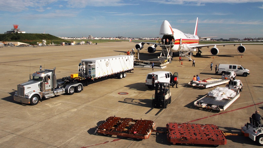 A containerized biocontainment system developed by Phoenix Air, center, is maneuvered into a Kalitta Air Boeing 747-400 cargo aircraft at Hartsfield-Jackson International Airport in Atlanta surrounded by additional hardware during preparation for a containment mission. Photo courtesy of Phoenix Air.