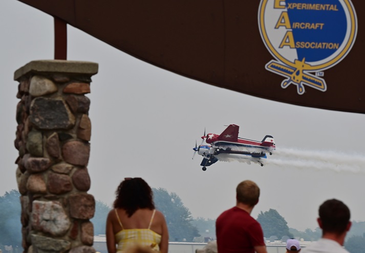 Attendees frame Jeff Boerboon in a jet-assisted Yak-110 as he performs near the brown arch during the EAA AirVenture afternoon airshow. Photo by David Tulis. 