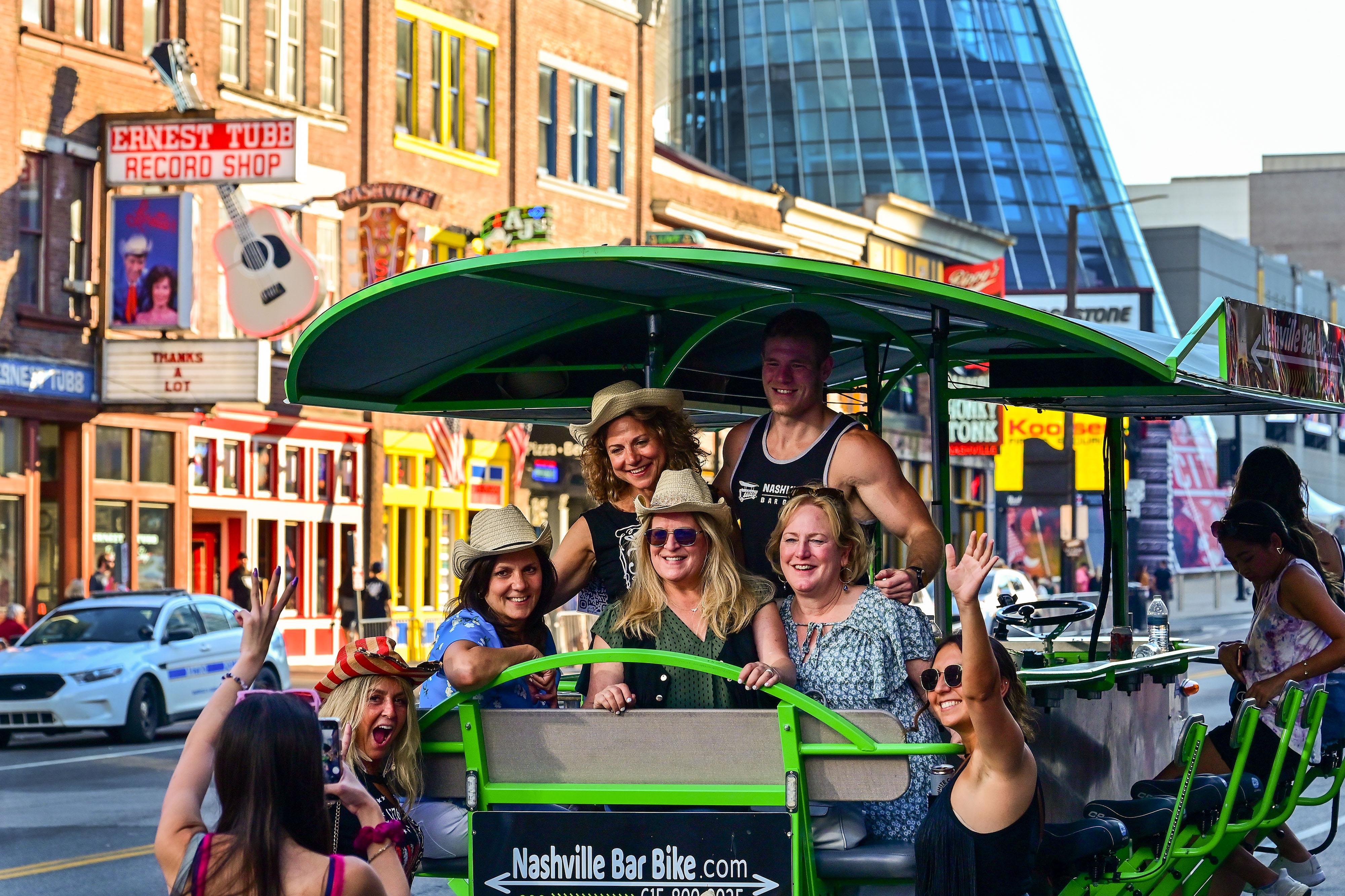 Partygoers take a break from pedaling a Nashville Bar Bike near the Bridgestone Arena, rear, and across the street from Ernest Tubb Record Shop. The pedaling bar moves through Broadway under human power. Photo by David Tulis.