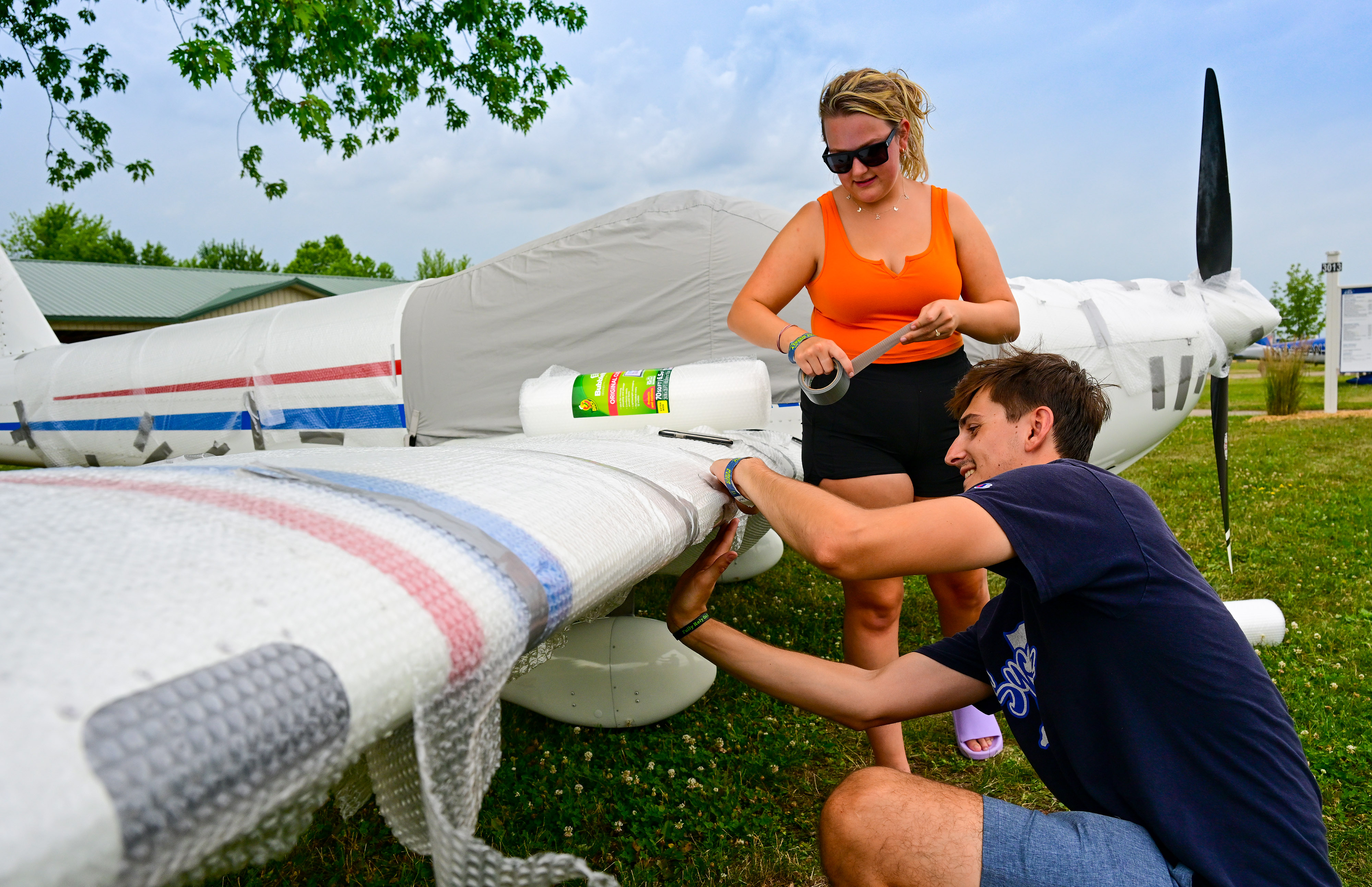 Van’s Aircraft RV-12 builder Madison Malcomb and her fianc&eacute; Dax Dausch apply bubble wrap to ward off potential damaging hail before a thunderstorm sweeps through Wittman Regional Airport as early arrivals and exhibitors hunker down during EAA AirVenture July 23, 2022. Photo by David Tulis.