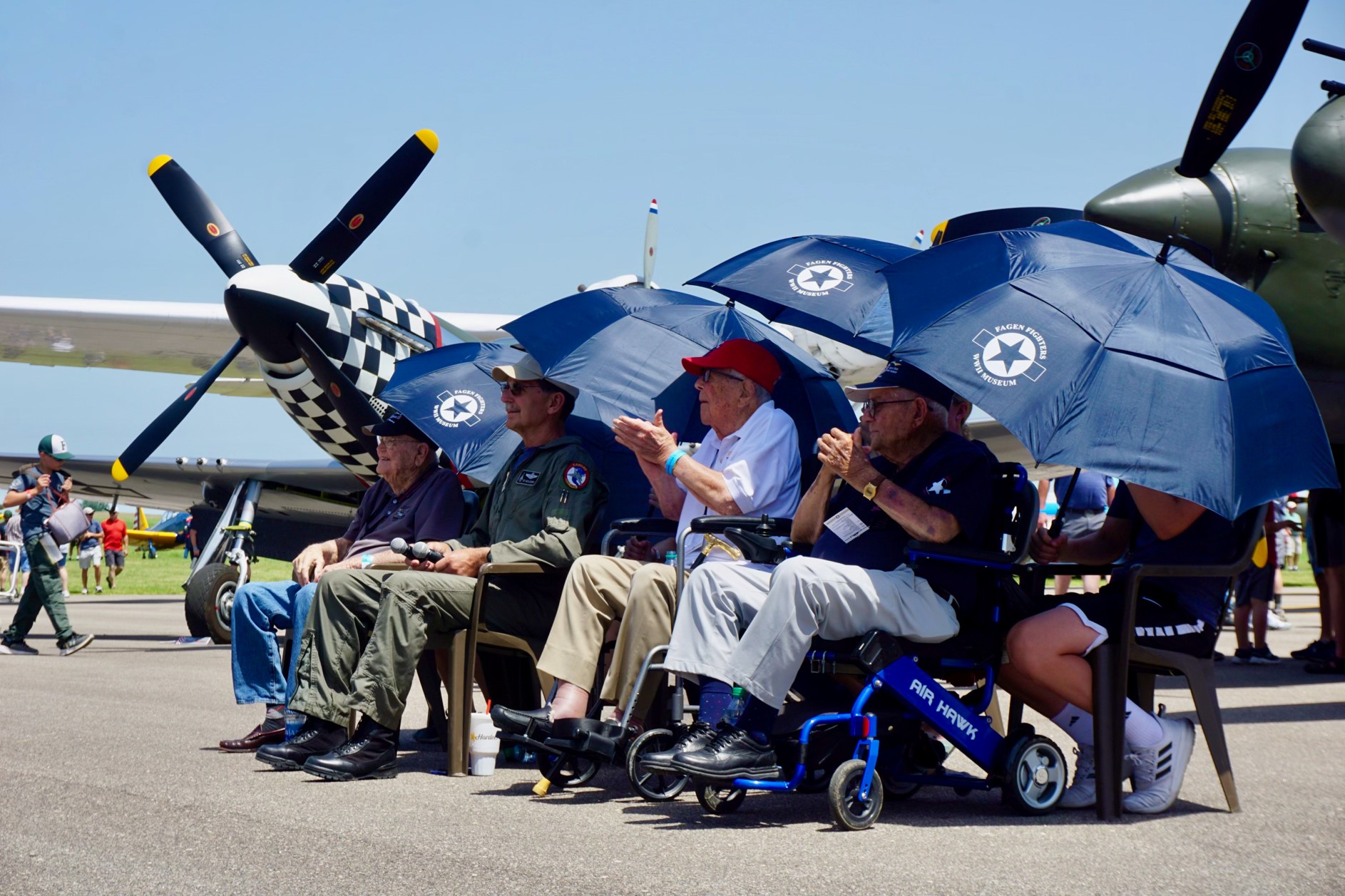 Left to right, Huie Lamb, moderator Edward Mcllhenny, Jim Tyler, and Donald McPherson sat on a panel to share their experiences as World War II fighter pilots with the crowd. The veterans were framed by their wartime airframes. Photo by Cayla McLeod Hunt.