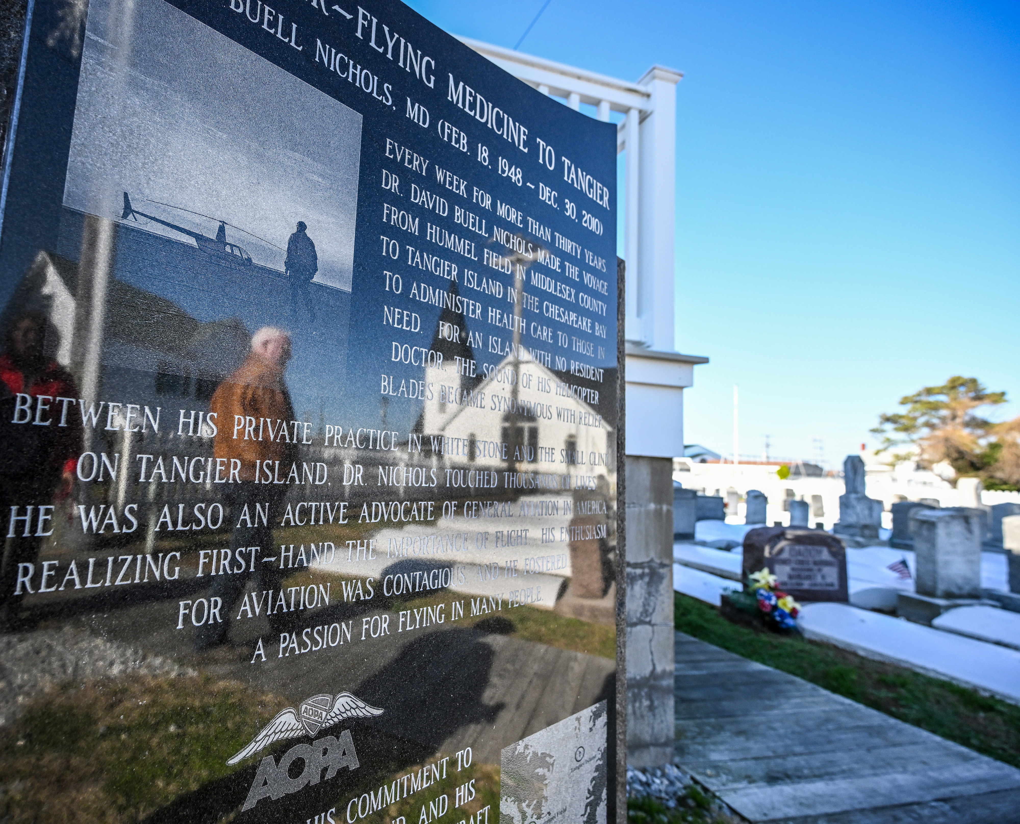 AOPA President Mark Baker is reflected in a plaque celebrating the life of 'Doctor Copter' and general aviation pilot David Nichols, who flew every week from the mainland to Tangier Island, to provide health care for its inhabitants. An island clinic was dedicated to Nichols, who died in 2010. Photo by David Tulis.