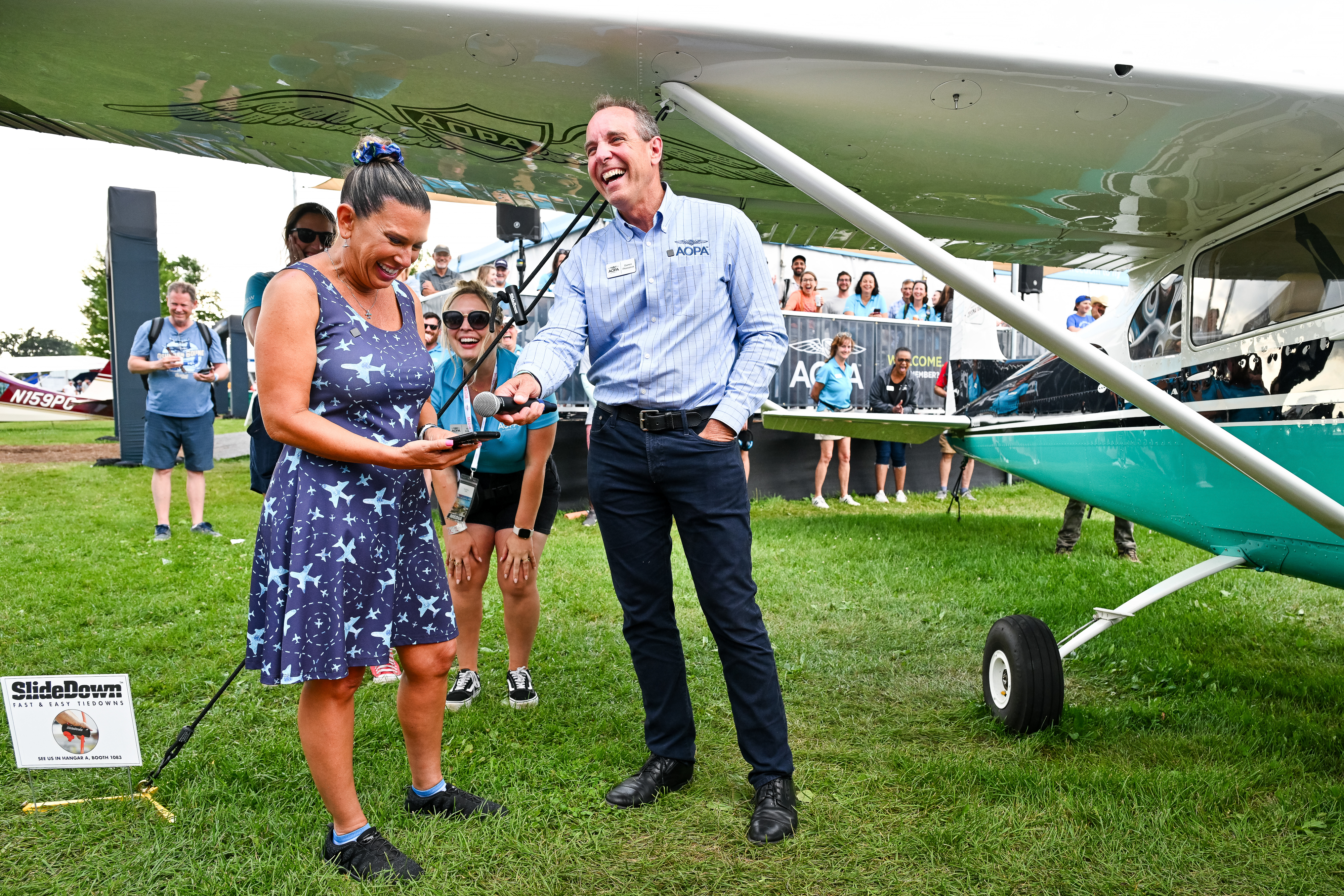 Jennifer Hortman calls her husband after winning the AOPA Sweepstakes Cessna 182 as AOPA President Darren Pleasance shares their conversation with the crowd. Photo by David Tulis.