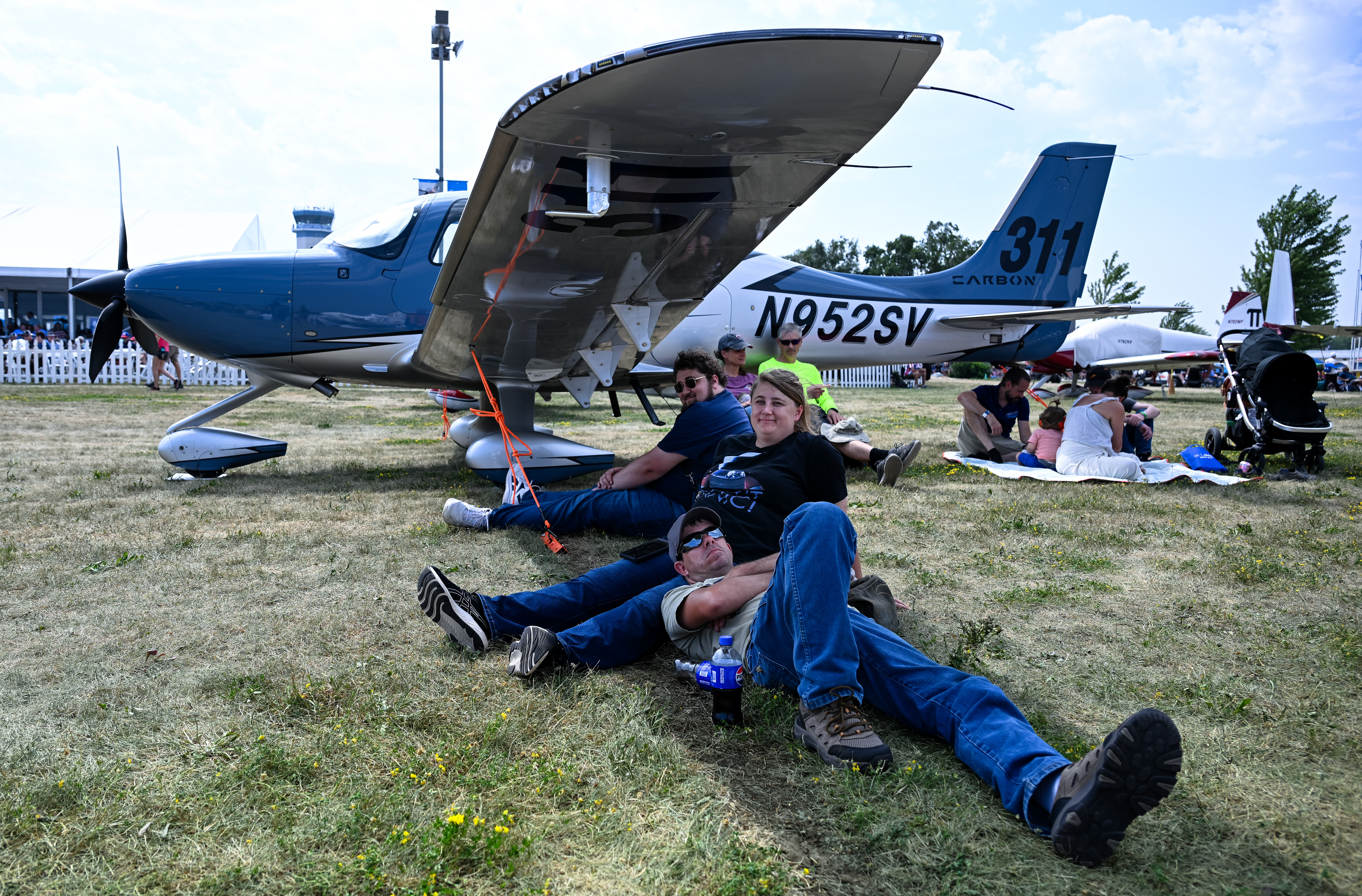 Attendees grab a shady spot under the wing of a Cirrus during the opening day airshow. Photo by David Tulis.