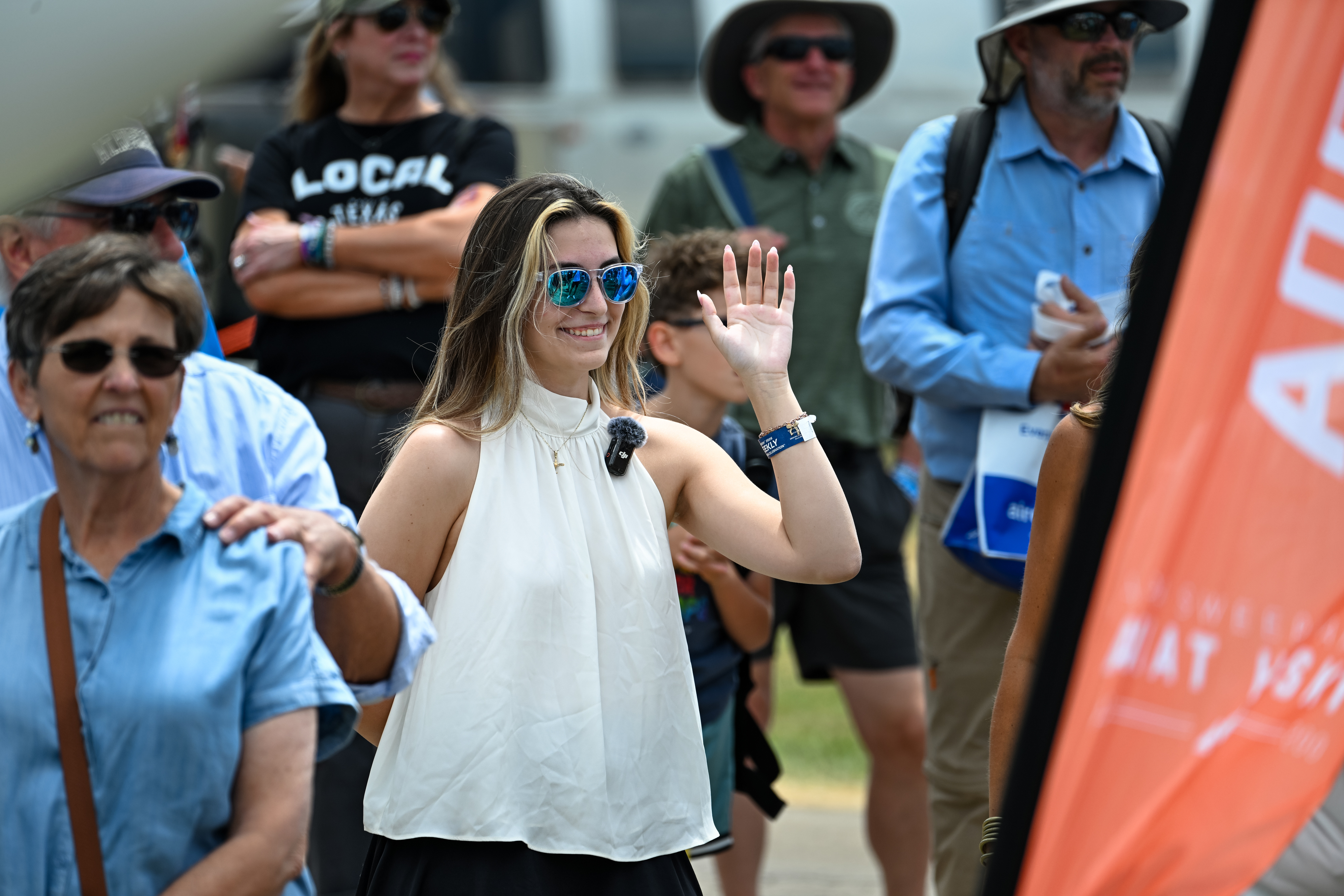 Pilot, flight instructor, and AOPA Sweepstakes Aviat Husky winner Ashley Almquist raises her hand during a ruse before accepting the aircraft at EAA AirVenture Oshkosh in Wisconsin on July 22. Photo by David Tulis.