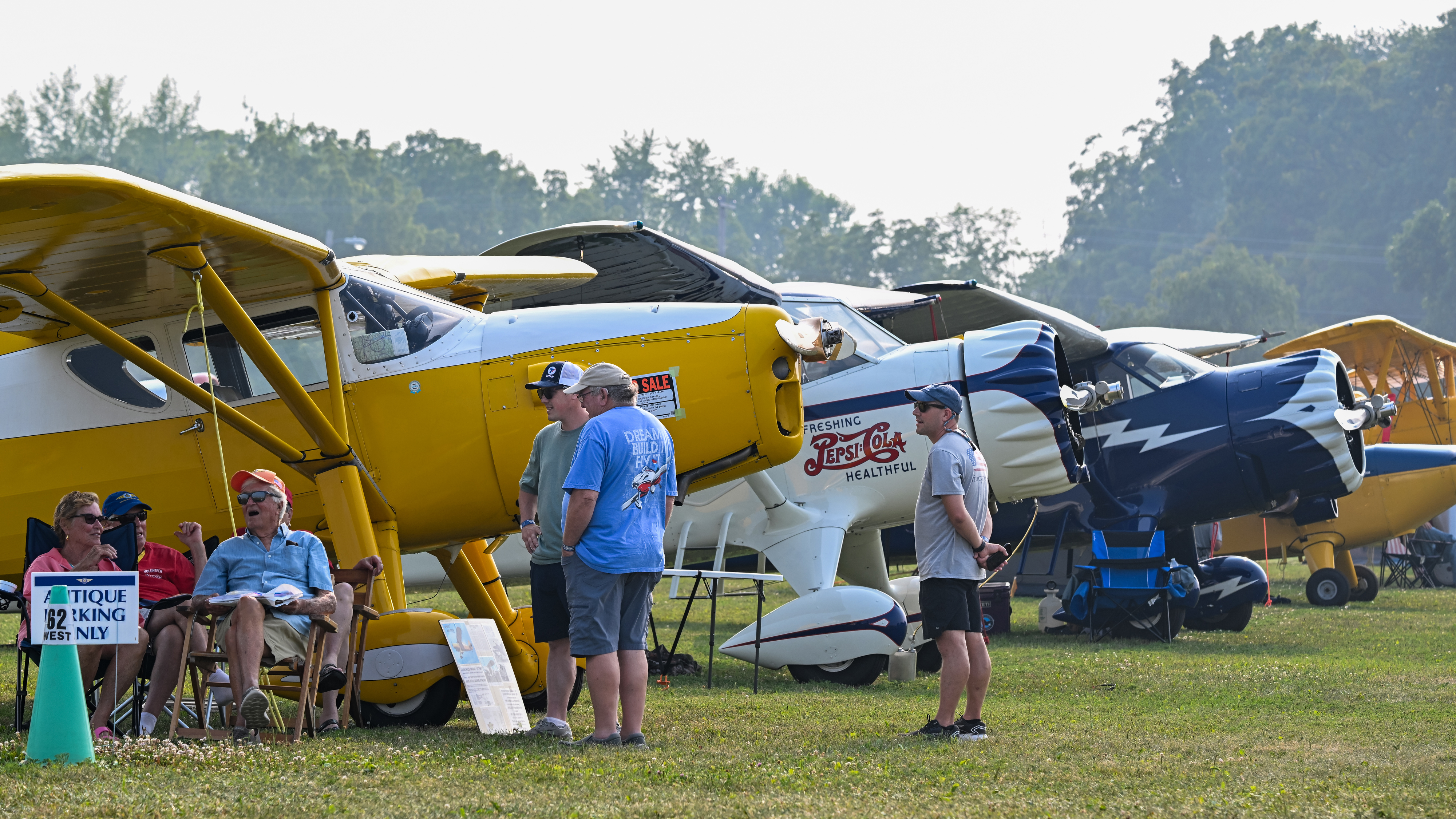 Attendees gather near vintage Stinson aircraft including a Reliant SR-7B gull-wing model with a Pepsi-Cola paint scheme during EAA AirVenture Oshkosh at Wittman Regional Airport in Wisconsin on July 18. Photo by David Tulis.