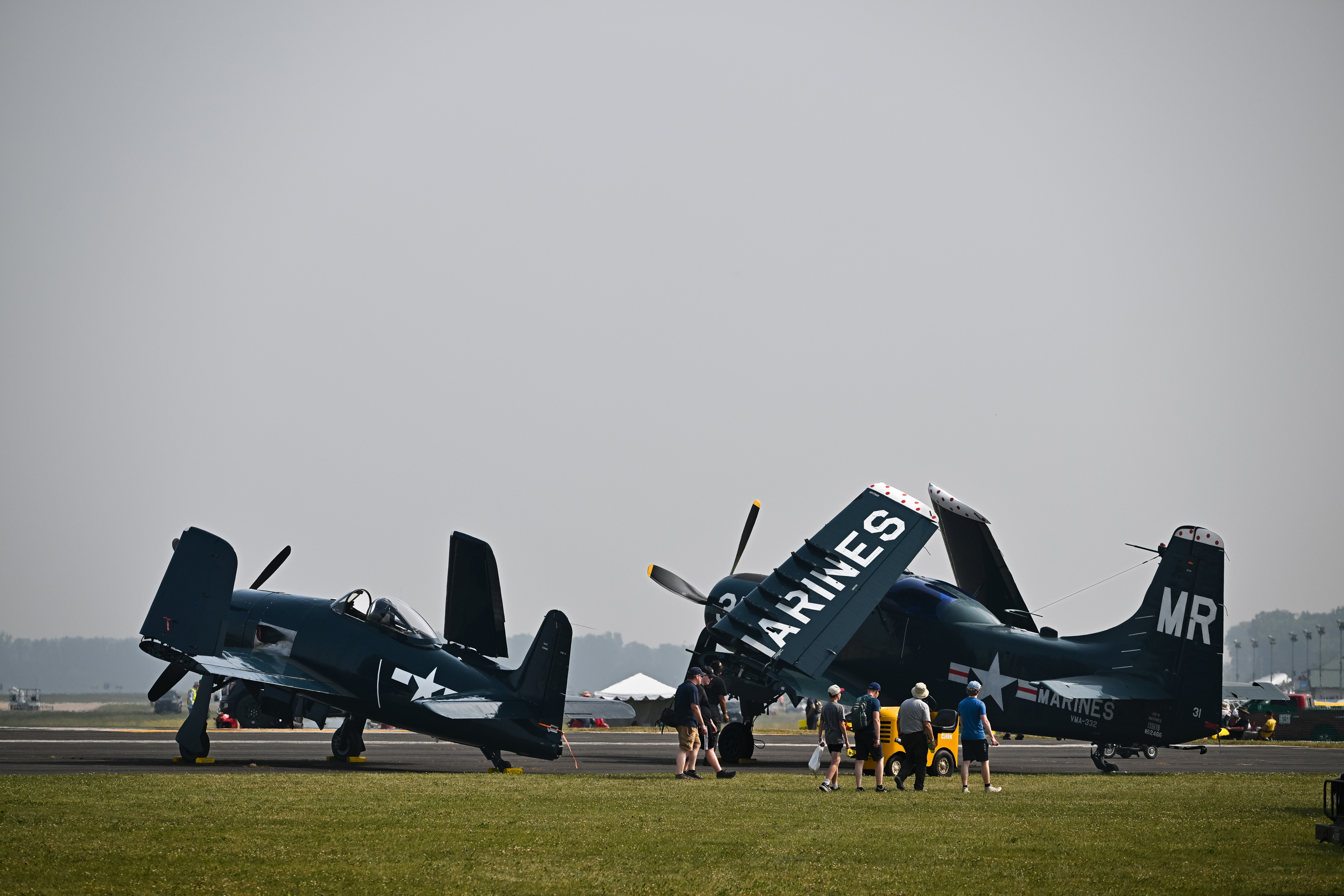 Smoke from Canadian wildfires paints the sky gray as airshow attendees walk past a folded-wing Douglas A-1 Skyraider on July 19. Photo by David Tulis.