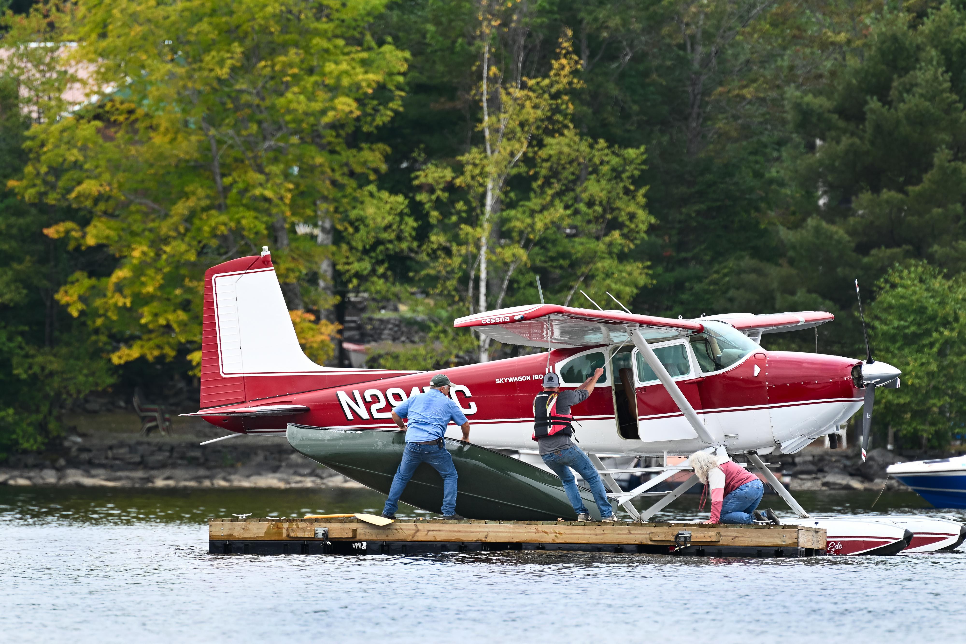 Tommy Dunn, left, lifts a canoe to the strut of his 1953 Cessna 180 floatplane as son Dustin, center, anchors the seaplane before the pair lash the canoe to the strut. Photo by David Tulis.