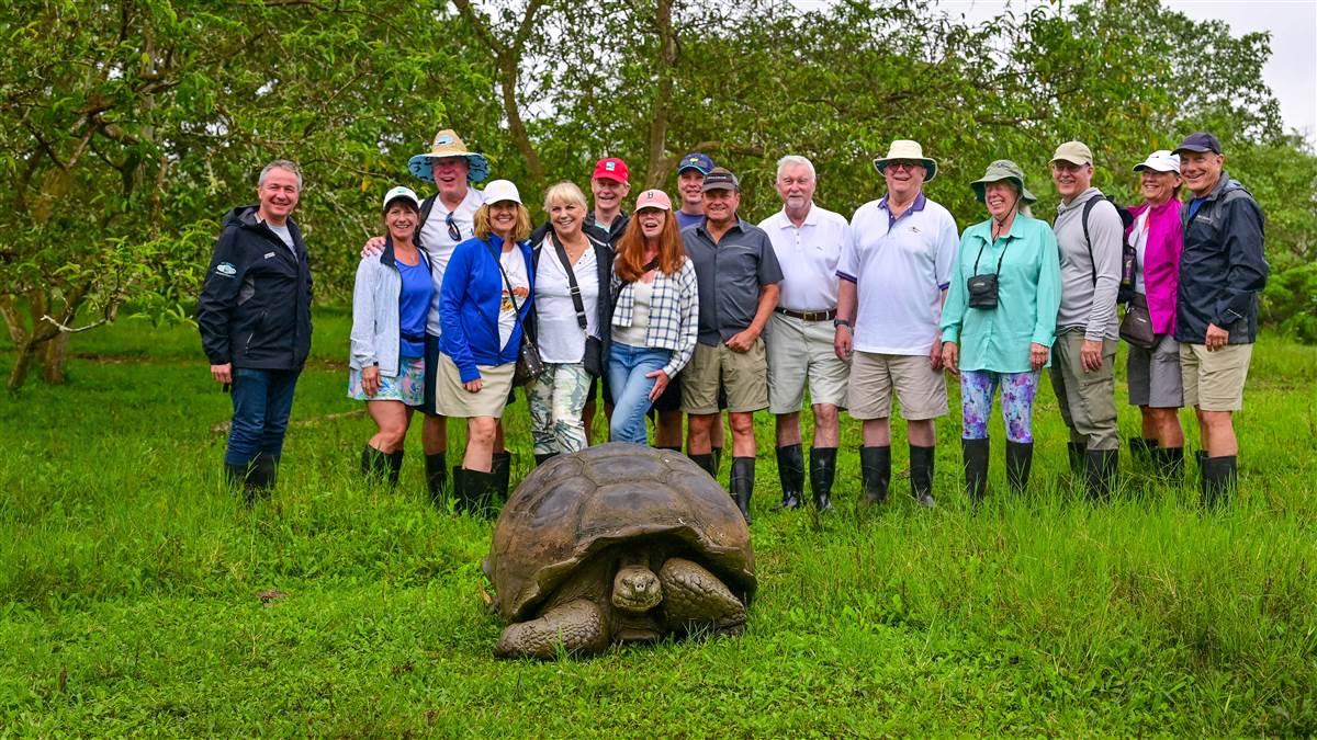 The group visits the El Chato Tortoise Reserve on Santa Cruz Island. Left to right: Christophe Mathy, Wendy Worden, Chris Worden, Beverly Taylor, Toni Kovacs, Allen Taylor, Linda Kocher, Walter Muharsky, Bob Kocher, Lou Kovacs, Tom Horne, Susan Dyer, Doug Dyer, Susan Dunsirn, Brian Dunsirn. Up front, a Galápagos giant tortoise.
