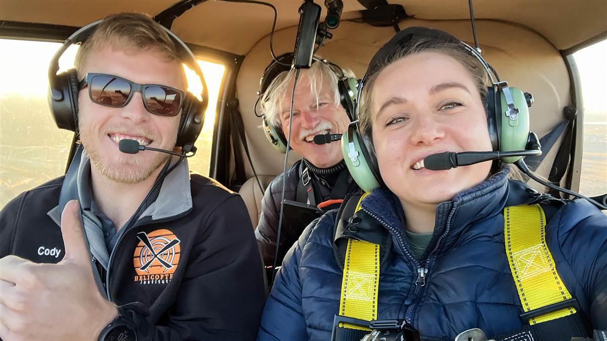 Senior Photographer David Tulis, Video Content Producer Michelle Walker, and Helicopter Institute Flight Instructor Cody Sargeant smile after a successful air-to-air mission with a Schweizer helicopter.; @michelle-walker
