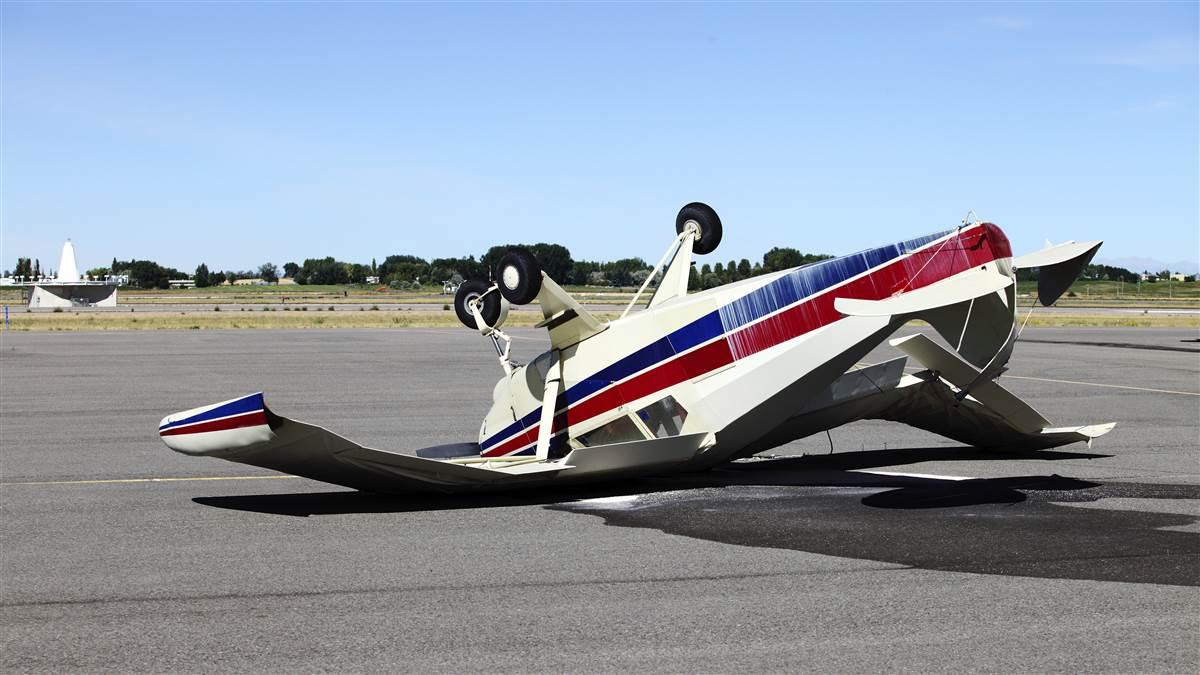 An mangled airplane resting upside down on the tarmac