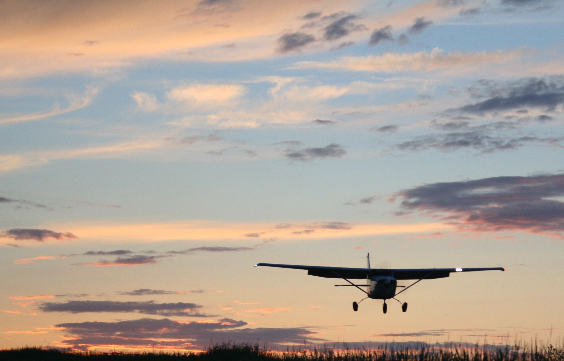 95736242 A single engine aircraft flying close to the ground near sunset.